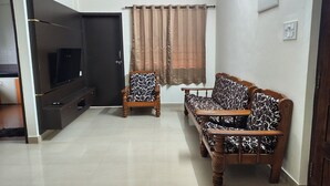 Un salón con televisor de pantalla plana, un sofá, una silla y una cortina.