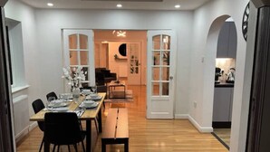A dining area with a wooden table set for four, flanked by black chairs. A bench is placed along the wall, and the room has a modern, clean design with white walls and wooden flooring. - Luxury 5-bed Bungalow w/ Hot Tub, Games & Parking (Dudley)