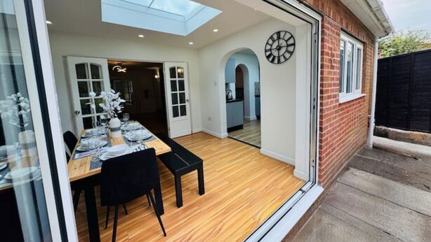 A dining area with a table set for four, a skylight above, and a clock on the wall. - Luxury 5-bed Bungalow w/ Hot Tub, Games & Parking (Dudley)