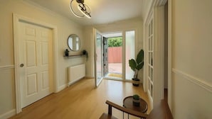 A hallway with wooden flooring, a white door, a mirror, and a small table with a plant. - Luxury 5-bed Bungalow w/ Hot Tub, Games & Parking (Dudley)