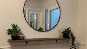 A round mirror on a wall with a wooden shelf below it. - Luxury 5-bed Bungalow w/ Hot Tub, Games & Parking (Dudley)