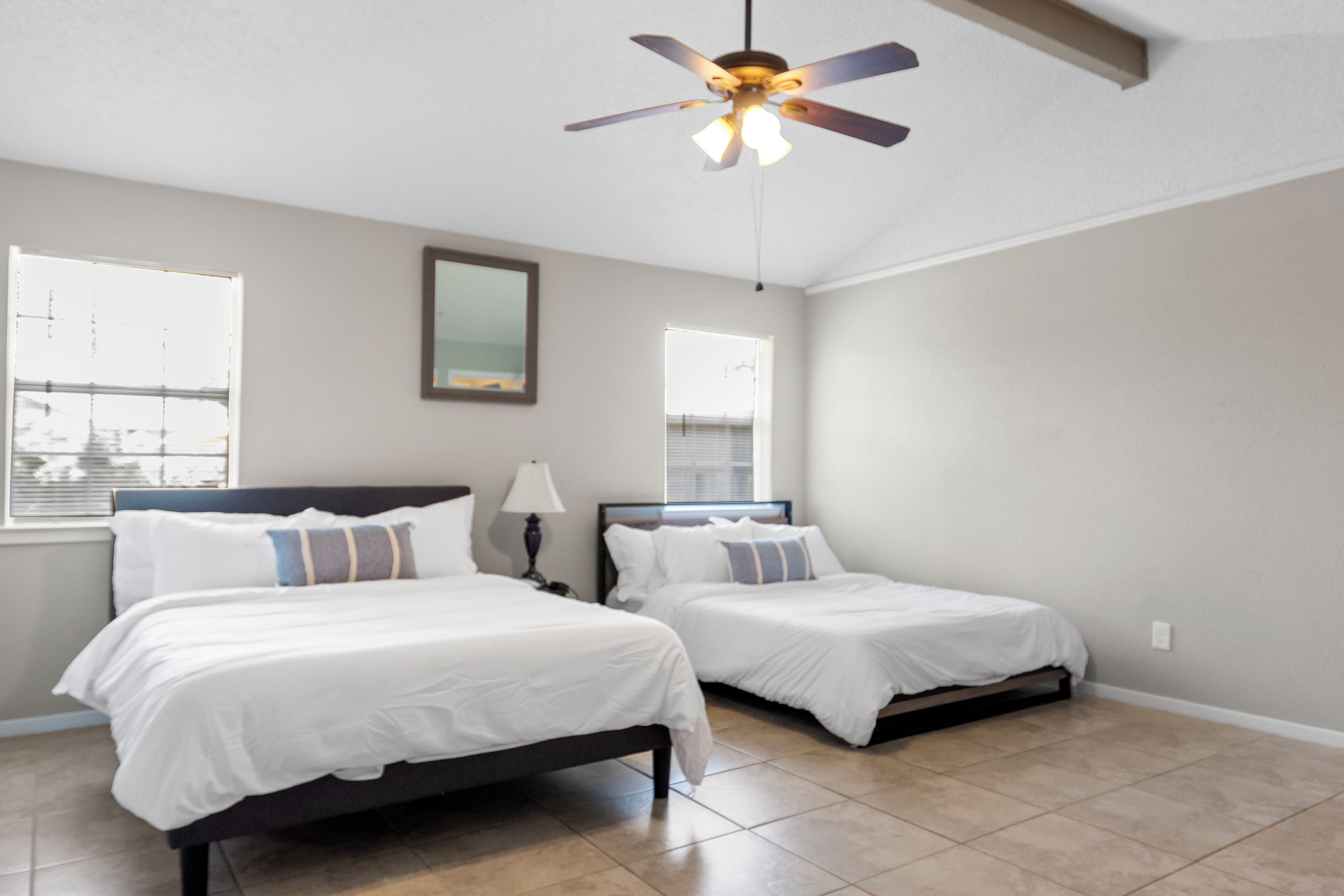 A bedroom with two beds, a ceiling fan, and large windows.