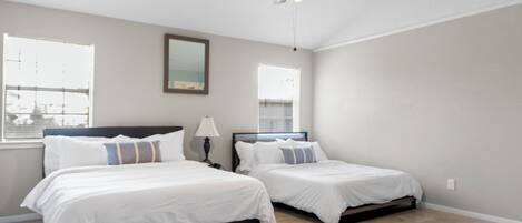 A bedroom with two beds, a ceiling fan, and large windows.