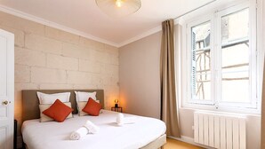 A bedroom with a large bed, two bedside tables, a window with curtains, and a brick wall.