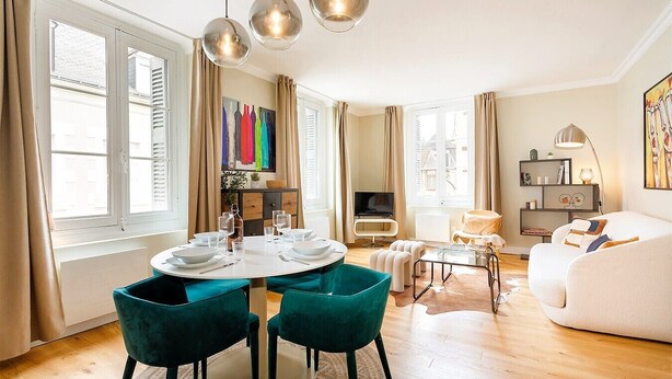 A modern living room with a round dining table, teal chairs, a sofa, and a TV.