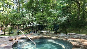 Un jacuzzi rodeado de baldosas de piedra, con barandilla y sillas de metal.