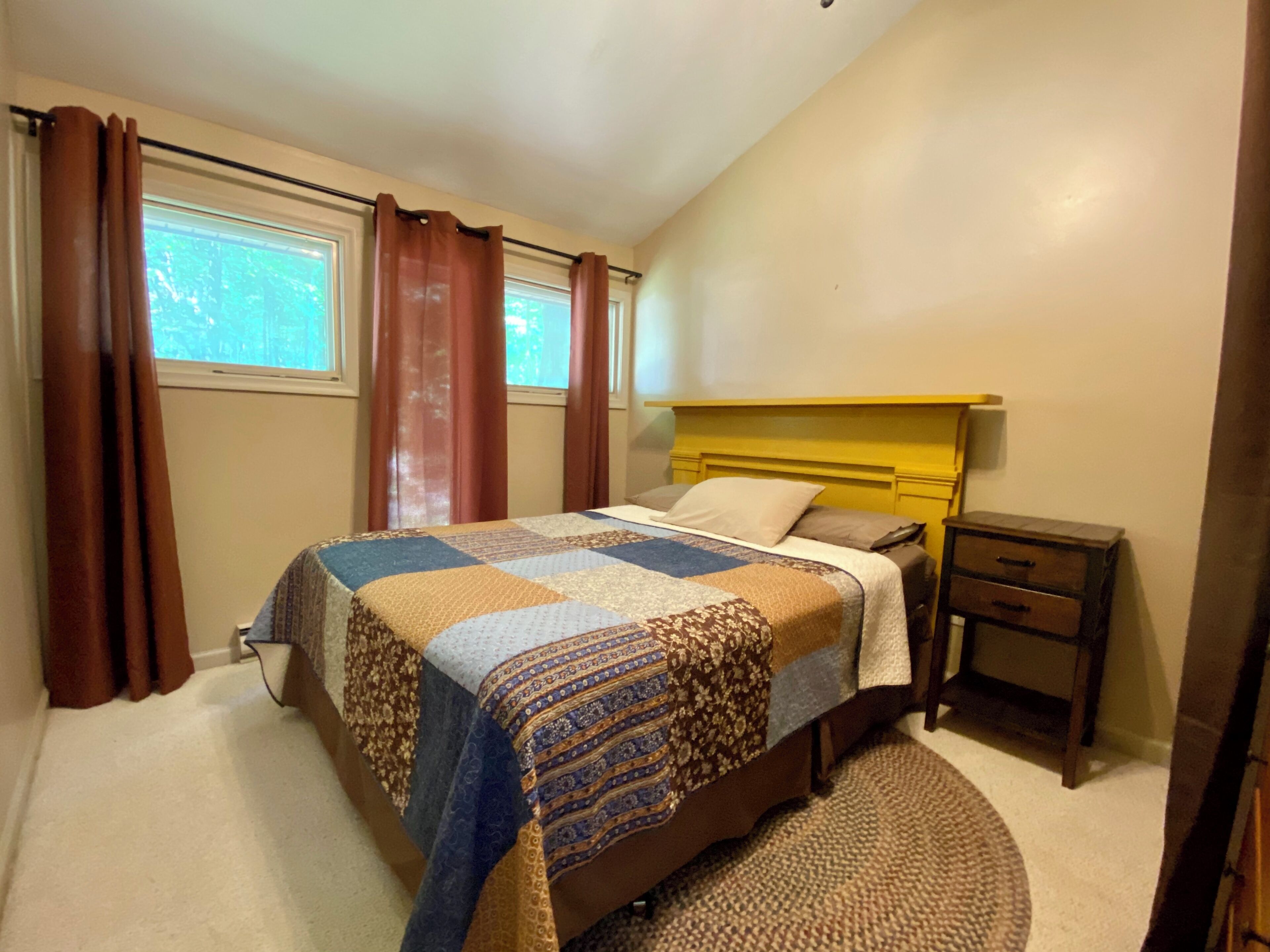 A bedroom with a bed, a nightstand, a window, and curtains.