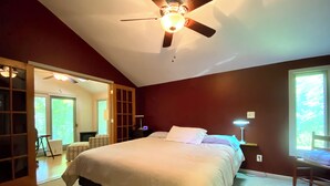 Une chambre avec un grand lit, un ventilateur de plafond et une fenêtre laissant entrer la lumière du jour.