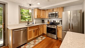 A modern kitchen with wooden cabinets, stainless steel appliances, a dishwasher, and a large window. - Lost Pines- Hot Tub | Pet Friendly | Family Friendly (Berkeley Springs)