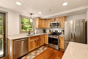 A modern kitchen with wooden cabinets, stainless steel appliances, a dishwasher, and a large window.