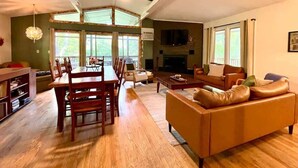 A spacious living room with a wooden dining table, leather sofa, and a fireplace. - Wildflower- Themed | Pet Friendly | Private Hottub (Berkeley Springs)