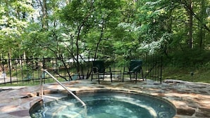 A hot tub surrounded by a stone patio, with a metal fence and chairs in the background. - Wildflower- Themed | Pet Friendly | Private Hottub (Berkeley Springs)