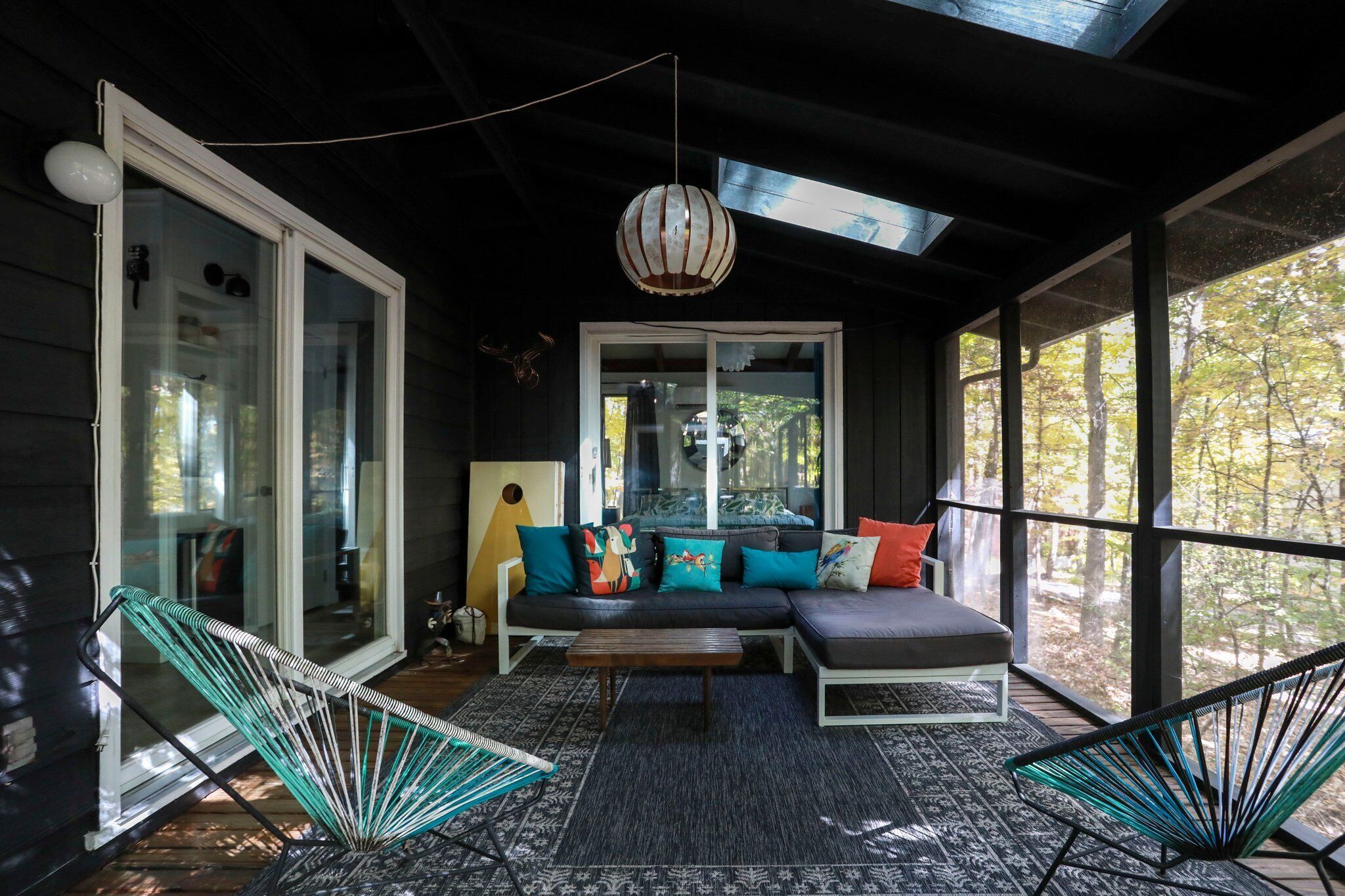 A cozy living area with a sofa, two chairs, a hanging light fixture, and a view of trees through large windows.