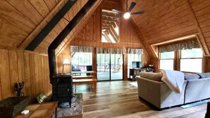 A cozy loft-style room with a high ceiling, wooden walls, a fireplace, a sofa, and a dining area.