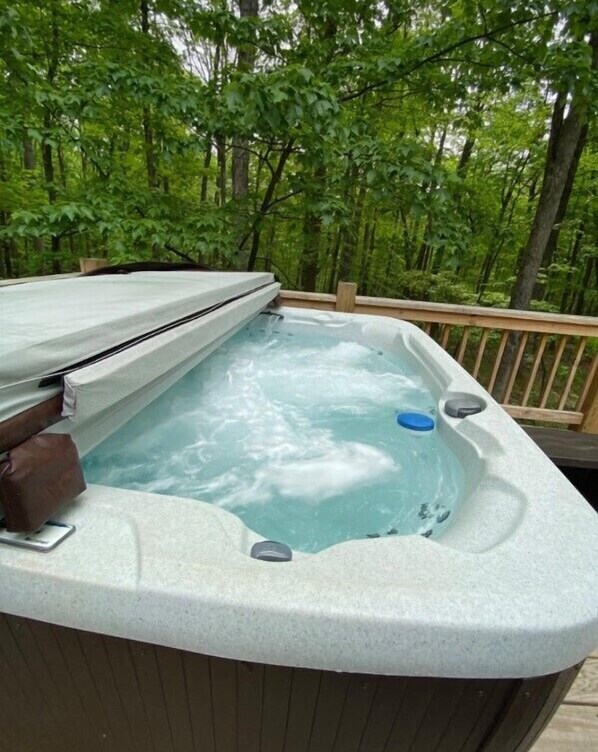 A hot tub on a wooden deck surrounded by trees.