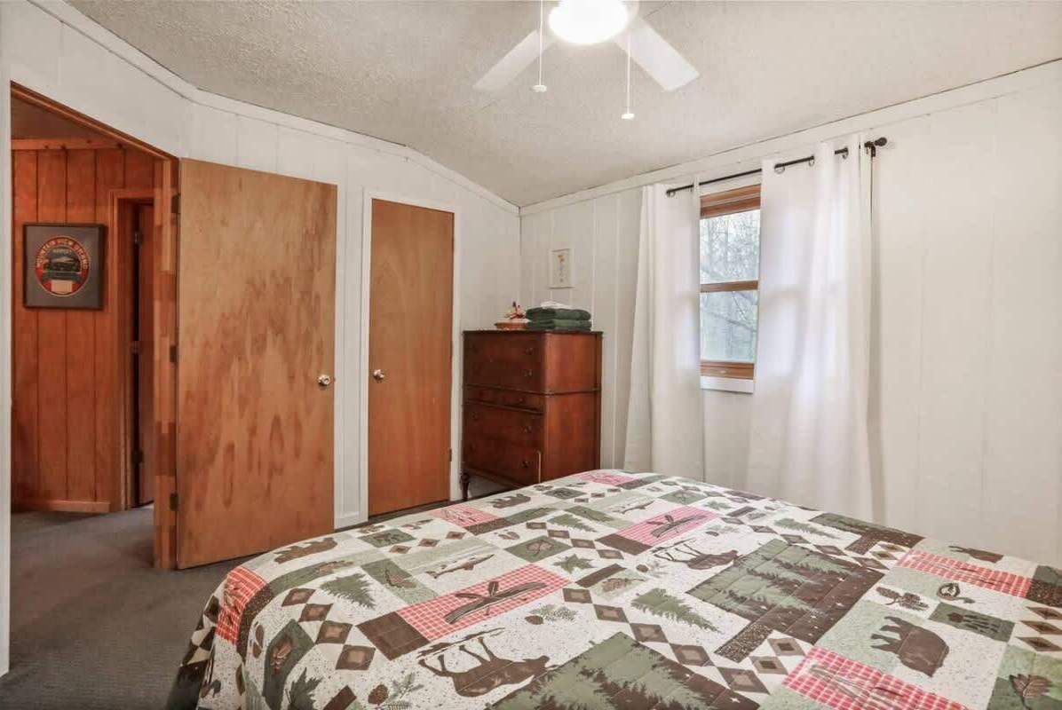 Une chambre à coucher avec une couvre-lit matelassé, une armoire en bois et un ventilateur de plafond.