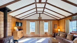 A cabin interior with a wooden interior, a fireplace, a sofa, and curtains. - "Evergreen" Private, creek-side escape (Berkeley Springs)