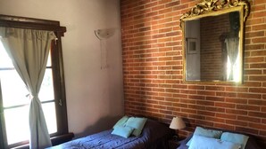 A room with two single beds, a window with curtains, a brick wall, and a mirror.