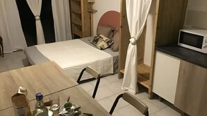 Ein kleiner, gemütlicher Raum mit einem Bett, einem Tisch mit Flasche und Gläsern, einer Mikrowelle und einem Schrank.
