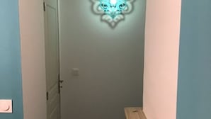 Ein schmaler Flur mit einer dekorativen Wandleuchte und einer kleinen Holzbank mit einem Teddybären darauf.