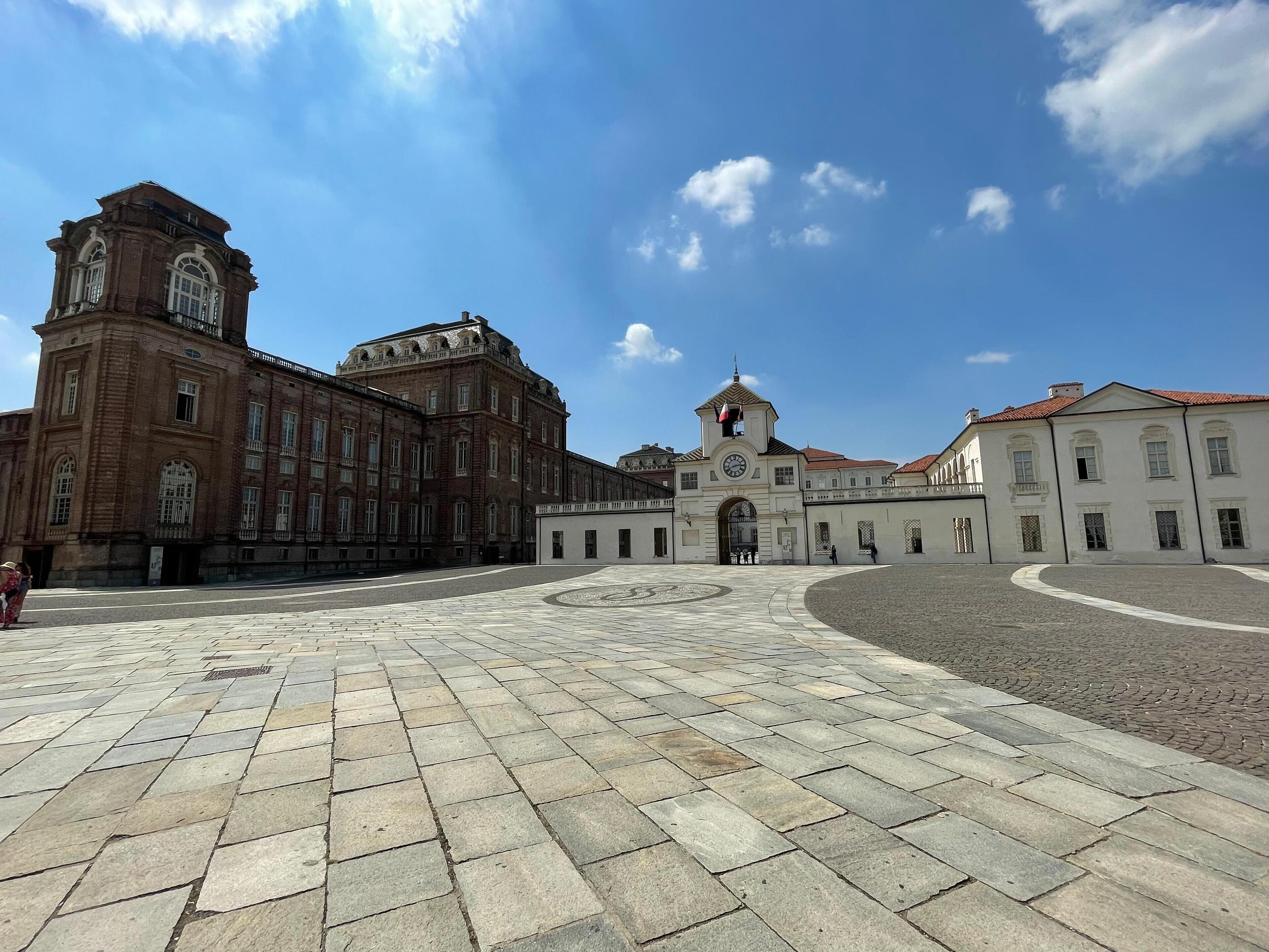 Un edificio histórico con una torre de reloj y un amplio patio central empedrado con losas de piedra.