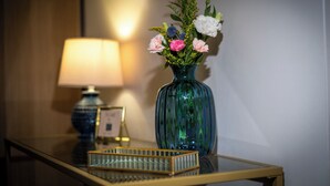 Un jarrón azul con flores sobre una mesa de vidrio, junto a una lámpara y un marco de fotos.