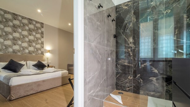 Un dormitorio moderno con una cama grande, una ducha con paredes de mármol y suelo de madera.