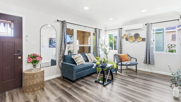 A modern living room with a blue sofa, a round coffee table, and a chair. There is a door with a mirror and a vase of flowers.