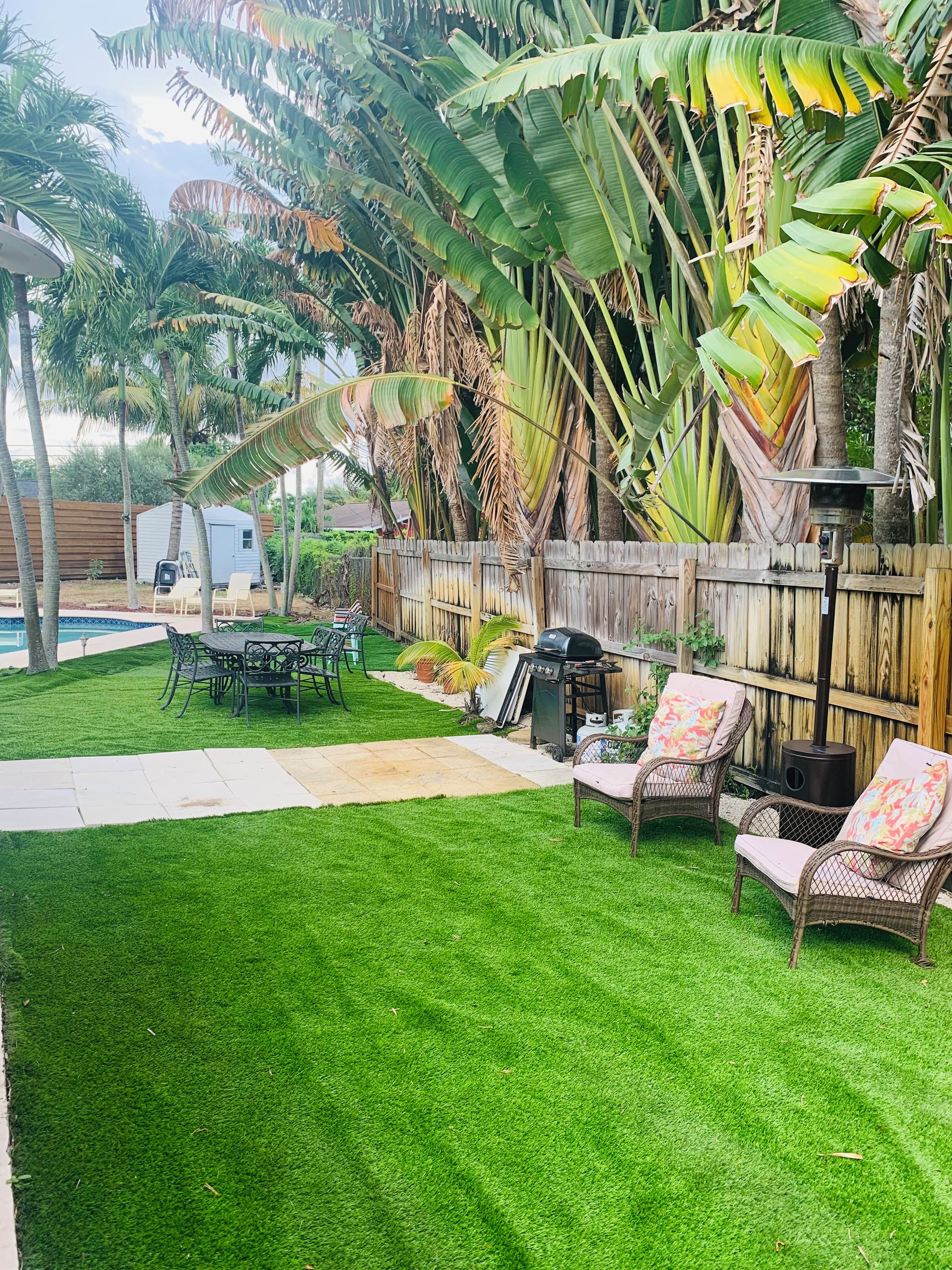 Un jardin avec une pelouse verdoyante, un barbecue, des meubles en osier et une clôture en bois.