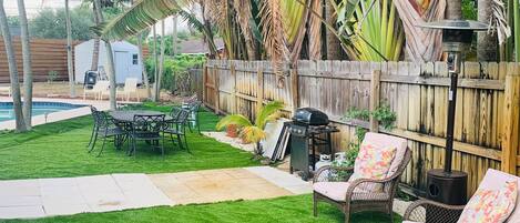 Un jardin avec une pelouse verdoyante, un barbecue, des meubles en osier et une clôture en bois.