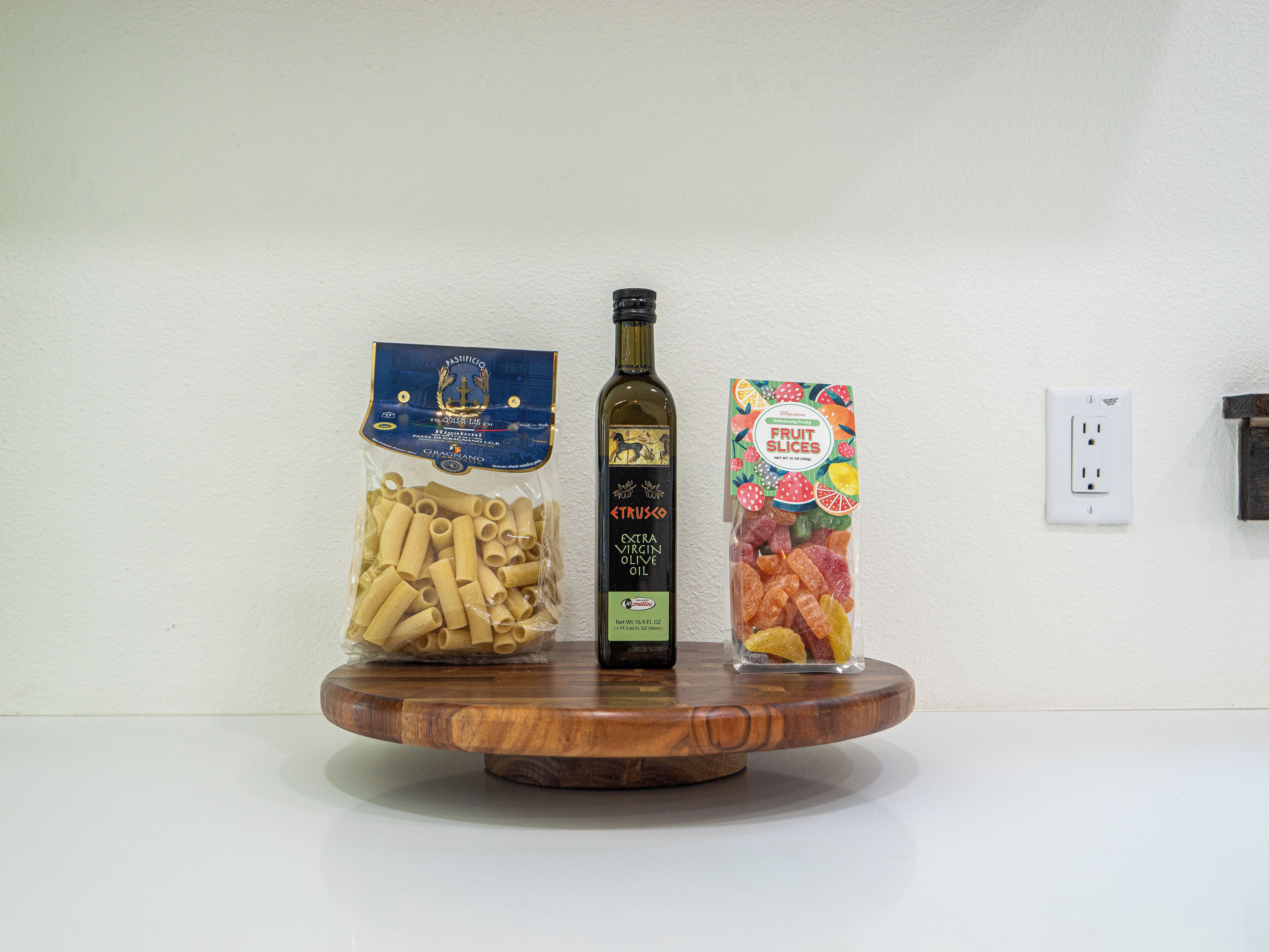 Un supporto in legno con tre elementi: pasta, olio d'oliva e fette di frutta.
