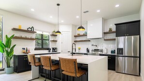 A modern kitchen with a central island, bar stools, a stainless steel refrigerator, and built-in shelves. - Beautiful Elegant New Tampa Luxury Home (Tampa)