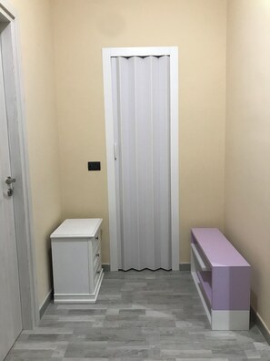 A narrow hallway with a white door, a white cabinet, and a purple bench.