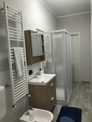 A modern bathroom with a white sink, a mirror, a towel rack, and a shower enclosure.