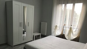 Et soveværelse med seng, skab, radiator og lette gardiner.