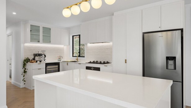Una cocina moderna con armarios blancos, un refrigerador de acero inoxidable, un horno empotrado y una isla grande con encimera de color claro.