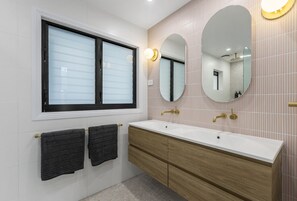 A modern bathroom with a large window, two mirrors, and a wooden vanity with a white sink.