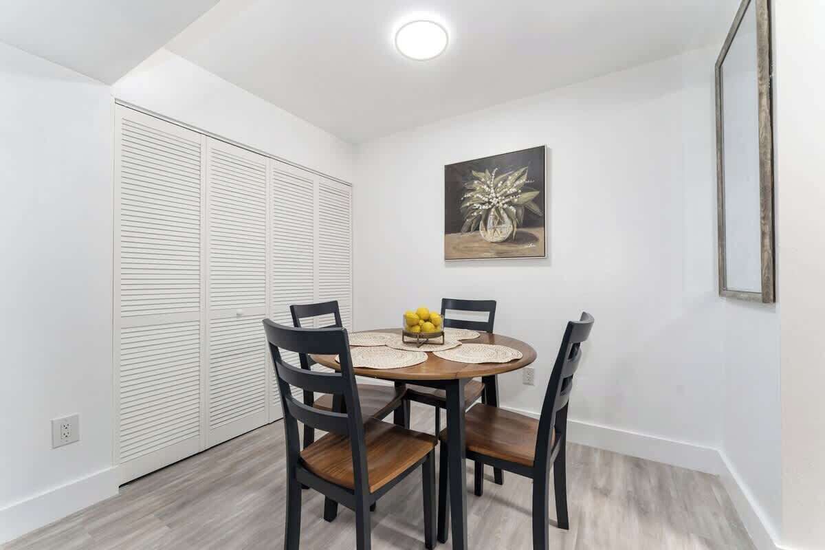 A dining area with a round table, four chairs, a fruit bowl, and a painting on the wall.