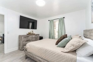 Ein Schlafzimmer mit einem Bett, einer Kommode, einem Flachbildfernseher und einem Fenster mit Vorhängen.