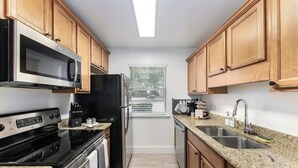 Cocina compacta con armarios de madera, microondas de acero inoxidable, refrigerador negro, estufa y lavamanos con encimeras de granito.