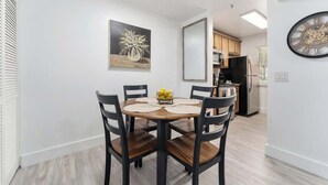 Un comedor con una mesa redonda, cuatro sillas, un frutero y un reloj en la pared.