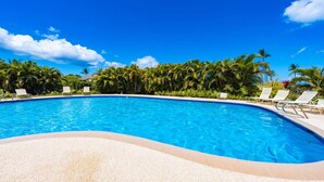 A clear blue swimming pool surrounded by palm trees and lounge chairs.