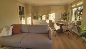Ein modernes Wohnzimmer mit einer Couch, einem Esstisch, Stühlen und Topfpflanzen.