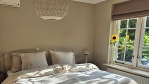 Ein Schlafzimmer mit einem großen Bett, einer Hängelampe, einem Fenster mit Blick ins Grüne und einer Heizung.