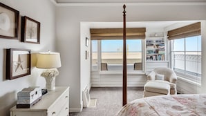 A bedroom with a four-poster bed, a window with a view of the beach, a bookshelf, and a dresser. - 5 bedroom Cottage on the Strand! (Hermosa Beach)