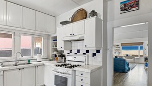 A modern kitchen with white cabinetry, a gas stove, and a large window overlooking the beach. - 5 bedroom Cottage on the Strand! (Hermosa Beach)