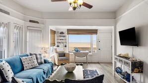 A living room with a blue sofa, a dining table, and a view of the beach through a large window. - 5 bedroom Cottage on the Strand! (Hermosa Beach)