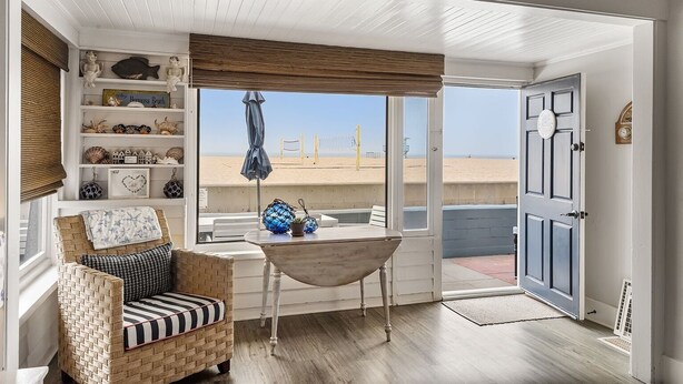 A beachside room with a wicker chair, a small table with decorative items, and a view of the beach. - 5 bedroom Cottage on the Strand! (Hermosa Beach)