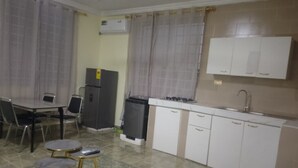 A compact kitchen with a dining area, including a table and chairs, a refrigerator, a sink, and cabinets. - Charming 1-bedroom apartment in Tema with AC (Tema)