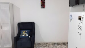 A room with a black armchair, a white wardrobe, a flat-screen TV mounted on the wall, and a patterned floor. - Charming 1-bedroom apartment in Tema with AC (Tema)